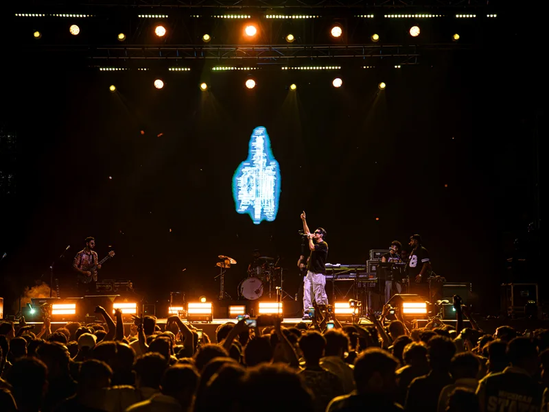 Wide concert view with a singer raising an arm beneath warm lights
