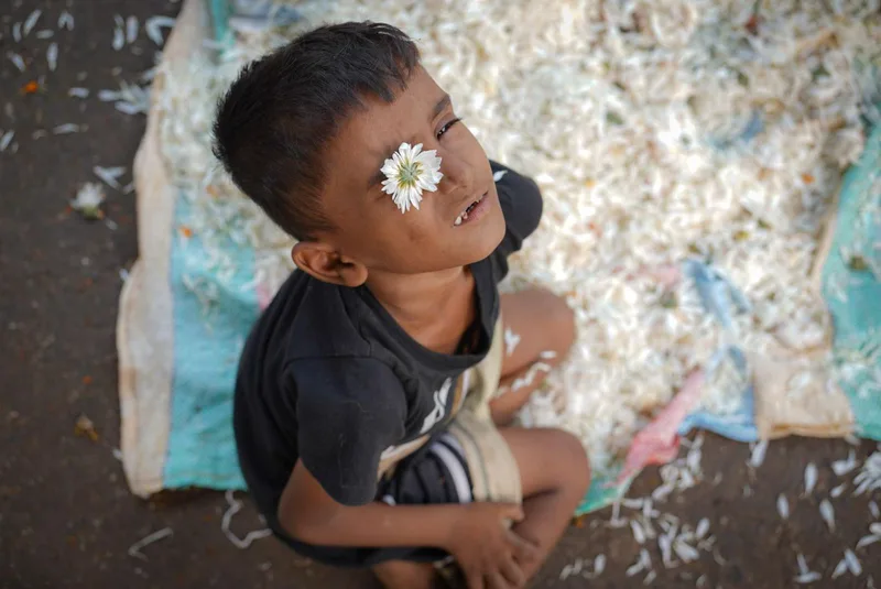 A child looking up with a white flower resting on their forehead